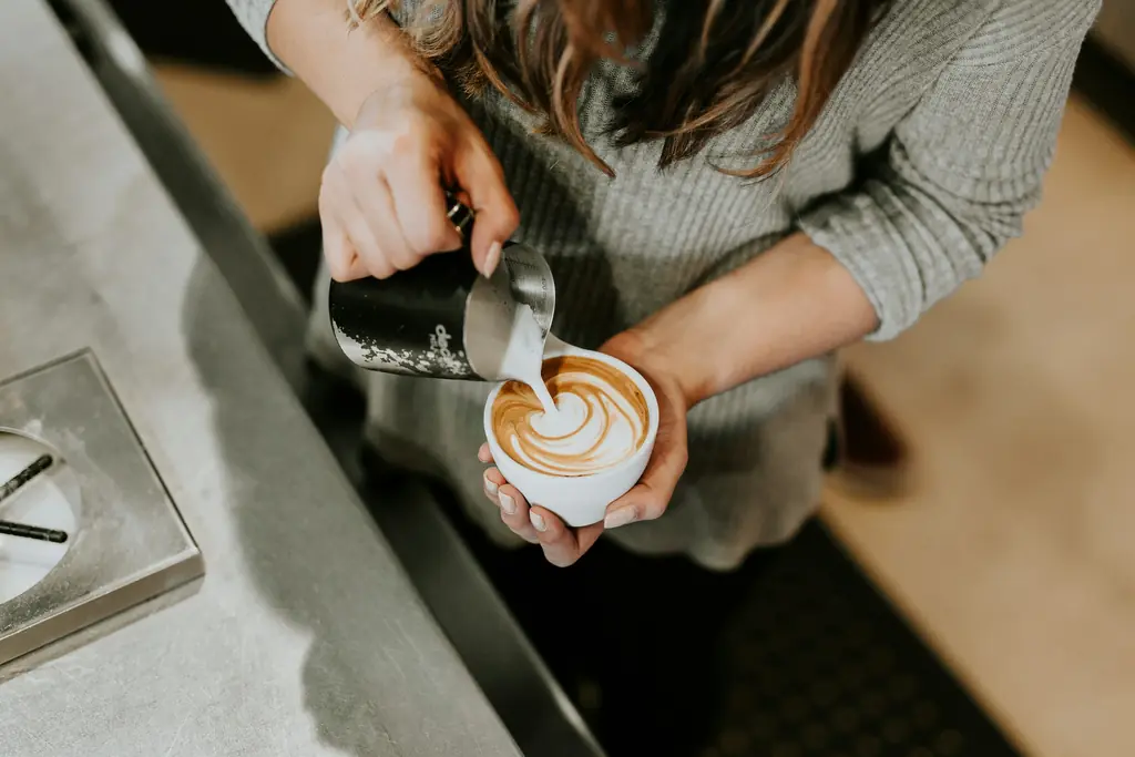 Una barista sirve leche sobre un café con arte latte.